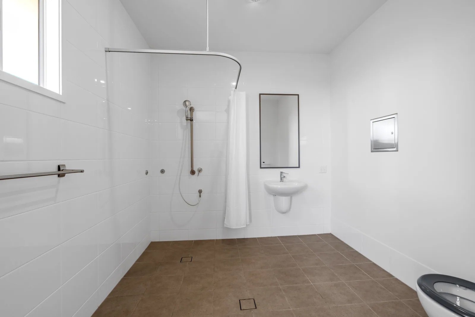 Accessible bathroom with a curtained roll-in shower and wall-hung basin